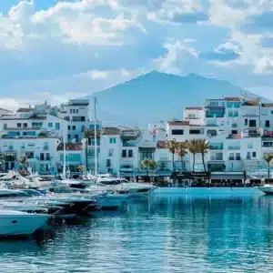 Luxury yachts in Puerto Banús marina with white buildings and a mountain backdrop under a blue sky, illustrating the high-end appeal for real estate investment in Spain.